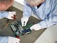 Electronics repair service technicians have circuit board on the work bench.